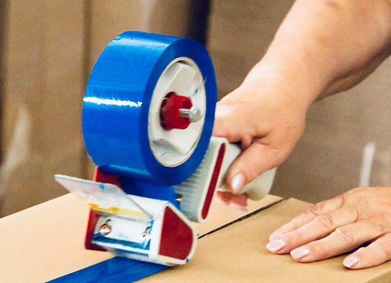 Woman in warehouse worker uniform packing cardboard box to delivery.