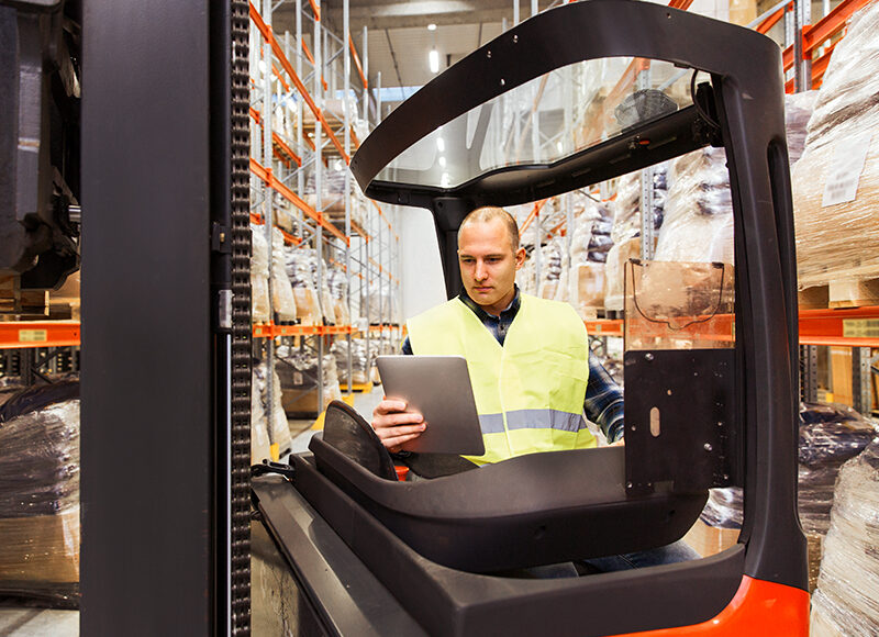 man with tablet pc operating forklift at warehouse