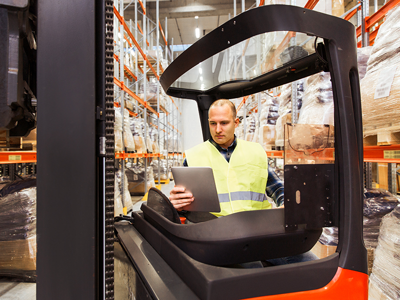 man with tablet pc operating forklift at warehouse
