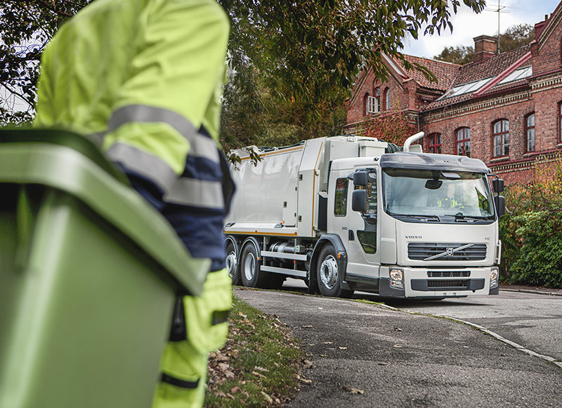 Renhållningsarbetare drar sopkärl mot sopbil.